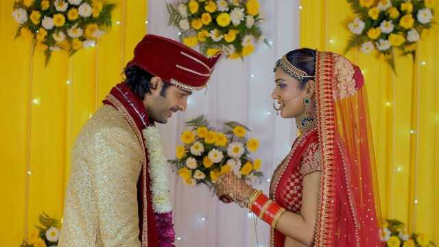 Attractive Indian bride and groom exchanging wedding garlands on stage. Handsome boy in Sherwani and pretty girl in Lehenga standing on a stage during their Jaimala ceremony - Hindu marriage