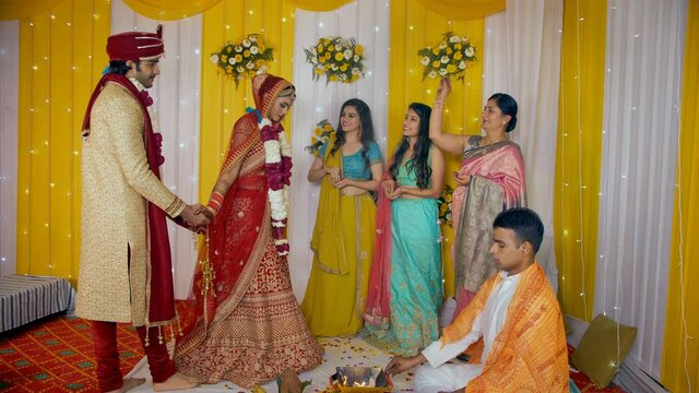 Indian bride and groom taking Pheras around the sacred fire while priest performing wedding rituals. Family/friends showering flower petals to bless the young couple - Indian marriage customs