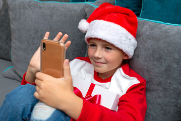 Handsome kid in Santa Claus hat looks at smartphone screen. Talk with family,closeup image.