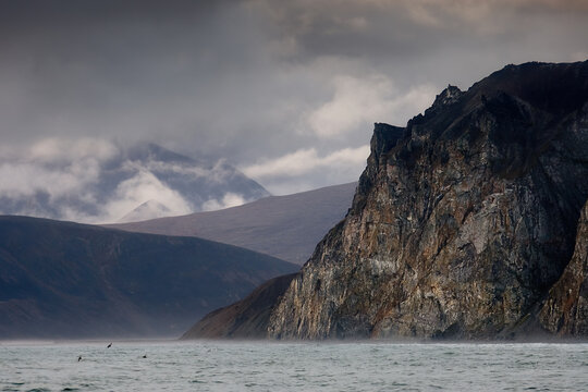 View of the rocks and mountains on the sea coast. Harsh arctic seascape. Gloomy cloudy autumn weather. Epic landscape. The nature of Chukotka and Siberia. Coast of the Bering Sea, Far East of Russia.