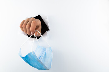 A female hand holds a medical mask through a hole in a white wall. Medical breakthrough concept,...