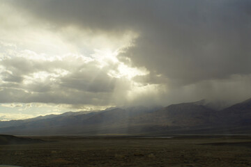 Moody landscape view of sun beams and rays breaking through storm clouds over Death Valley