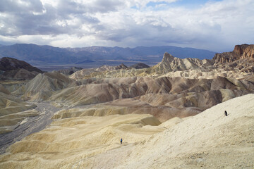Fototapeta premium A crow and a hiker in the distance, exploring the badlands terrain, as seen from Zabriskie Point in Death Valley National Park