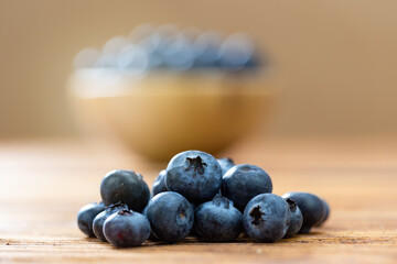Heap of fresh blueberries lying on wooden table. Pile of little raw blue berries on woody structured desk with full bowl in background. Small healthy fruit on focus.