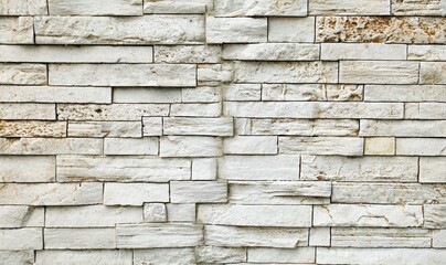 Old Stone wall cladding made of horizontal white bricks with brown spots, of natural rock stacked . Background and texture	