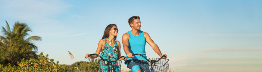 Obraz premium Biking tourists couple cycling enjoying summer outdoor sport activity banner panoramic. Young woman and man riding bicycles on Caribbean vacation. Active people lifestyle happy.
