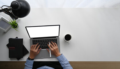 Top view image of businessman hand typing on white blank screen computer laptop at white working...
