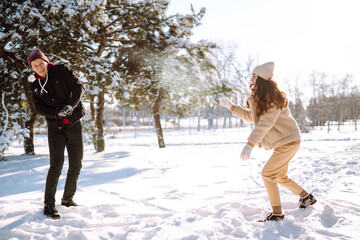 Fototapeta na wymiar Happy Couple in love walking and having fun in snow forest. Young man and woman playing in the snow on winter holidays. Christmas, New year. Winter lifestyle.