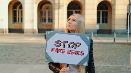 Young woman protesting against fake news. She walking down the street with placard.