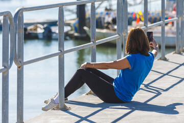 young girl sitting on a pier taking a picture with the mobile phone