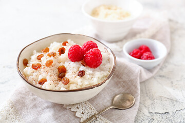 Bowl of tasty rice pudding with raspberry and raisins on light table