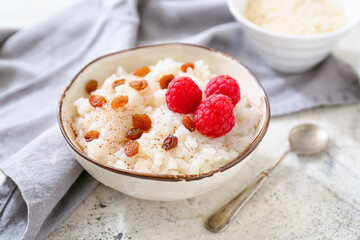 Bowl of tasty rice pudding with raspberry and raisins on light table