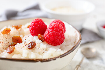 Bowl of tasty rice pudding with raspberry and raisins on light table