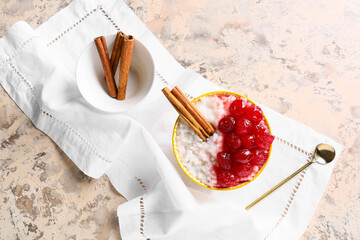 Bowl of tasty rice pudding with cherry and cinnamon on white napkin