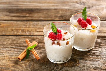 Glass cups of tasty rice pudding with raspberry and raisins on wooden table