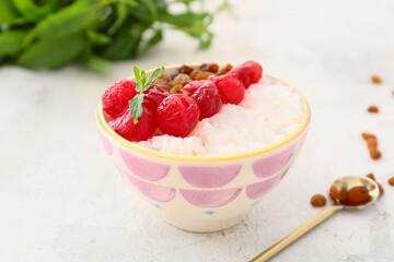 Bowl of tasty rice pudding with raspberry and raisins on white table