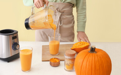 Woman preparing tasty pumpkin smoothie at table