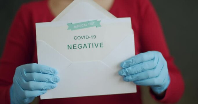 Woman Holding Negative Antigen Detection Test for Covid-19. Push In of Unidentifiable Person Wearing Face Mask and Blue Surgical Gloves Showing Open Envelope with Negative Coronavirus Test Results.