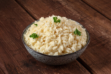 A bowl of cooked rice on a rustic wooden table, served with fresh parsley