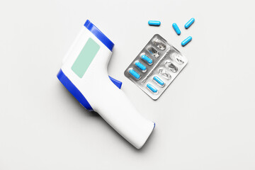 Infrared thermometer and pills on light background