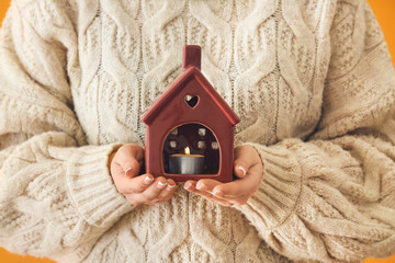 Woman holding figure of house with burning candle, closeup. Concept of heating season