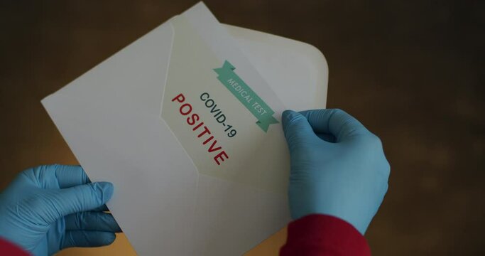 Person Pulling Certificate with Positive Results in Covid-19 from Envelope. Closeup of Person Wearing Surgical Gloves Slowly Pulling Positive Test Results in Coronavirus from Opened Envelope.