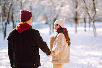 Happy couple hugging and kissing outdoors in winter park. Young man and woman enjoy each other in snow forest. Holidays, season, love and leisure concept.