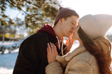 Happy couple hugging and kissing outdoors in winter park. Young man and woman enjoy each other in snow forest. Holidays, season, love and leisure concept.