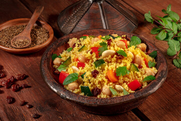 Moroccan couscous in a tagine with ingredients on a dark rustic wooden background