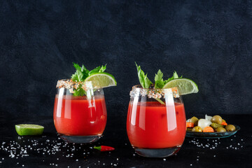Bloody Mary cocktails on a dark background with copy space, a side view. Tomato juice and alcohol mix, garnished with lime and celery