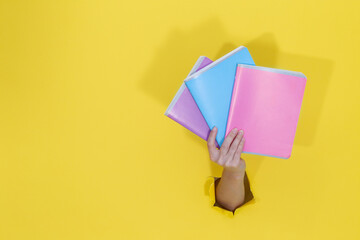 Female hand holding colorful notebooks from yellow torn paper. Back to school Education concept. School stationery and office supplies. Space for text.