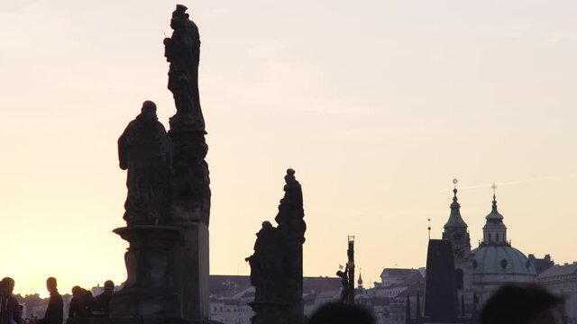 large baroque statues silhouette decorate famous Charles Bridge against picturesque cityscape with church spires in twilight