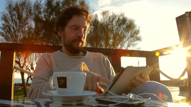 Man relaxing in the morning in front of the sea smiling looking camera reading tablet