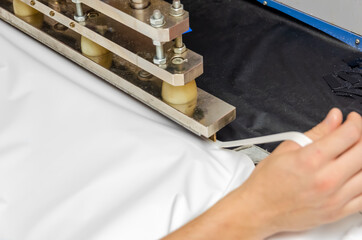 Men's hands work at the machine for welding PVC film and edging seam. Shop for the production of stretch ceilings.