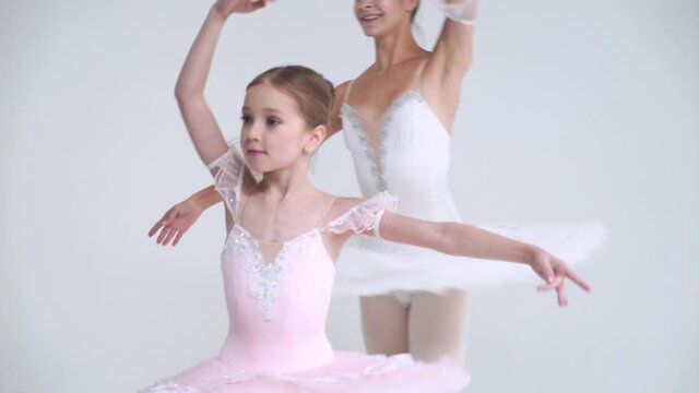 Young female and little girl in a white tutu, dance ballet and perform choreographic elements on a white background, rehearsal.