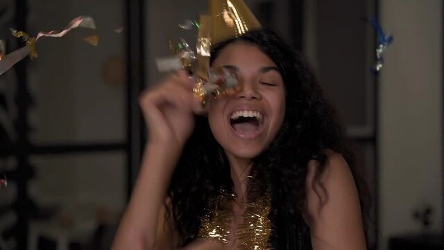 Portrait of a beautiful black woman making funny faces, dancing, throwing confetti at New Year's Eve party. African american female celebrating Christmas at home. 