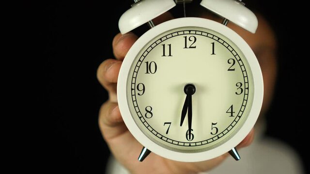 6:30 o'clock. Human hand holding alarm clock that showing six-thirty o'clock and ringing.