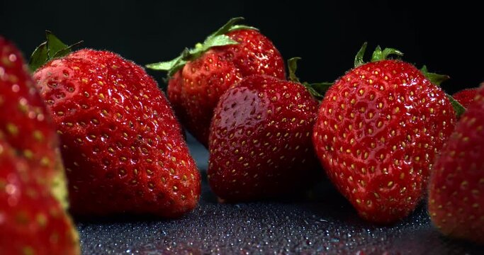 Strawberries close-up. Macro shot of strawberries on black background. Red ripe organic strawberries with sliding backward camera shot. High quality 4k footage