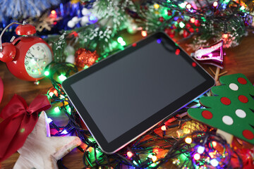 Digital tablet lying on table among sparkling garlands and New Year's toys closeup. Christmas discounts concept