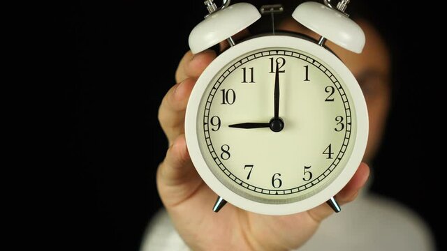 9 o'clock. Human hand holding alarm clock that showing nine o'clock and ringing.