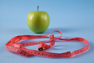 Whole green apple with measuring tape isolated on blue background.