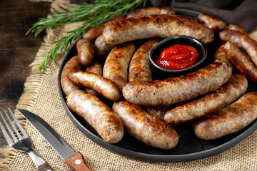 Fried sausages. Bavarian and Nuremberg sausages with spices and sauce. Delicious meat sausages in a black ceramic plate on a brown wooden table. German dish