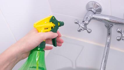 female hand in a rubber glove holding a spray for cleaning surfaces