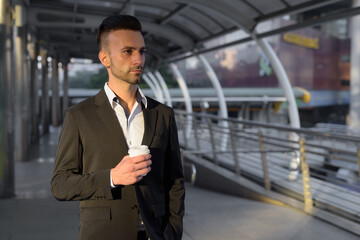 Businessman outdoors in city holding coffee cup while thinking