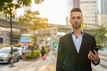 Businessman in city waiting taxi while using mobile app with phone