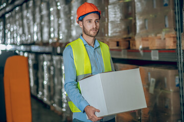 Young male worker carrying a box and looking serious