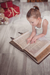 Weihnachten hübsches kleines Mädchen im weißen Kleid liest in einer alten Bibel Weihnachtsbaum,...