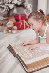 Fototapeta na wymiar Weihnachten hübsches kleines Mädchen im weißen Kleid liest in einer alten Bibel Weihnachtsbaum, Geschenke Var. 3