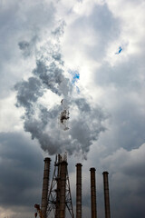 The silhouette of industrial pipes that smoke and release toxic waste against a blue sky with clouds. Dramatic harmful emissions, poor environmental ecology and global warming concept.