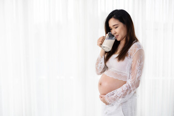 pregnant woman drinking a milk at the window in bedroom